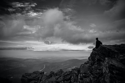 积云下坐在山顶上的人的灰度照片